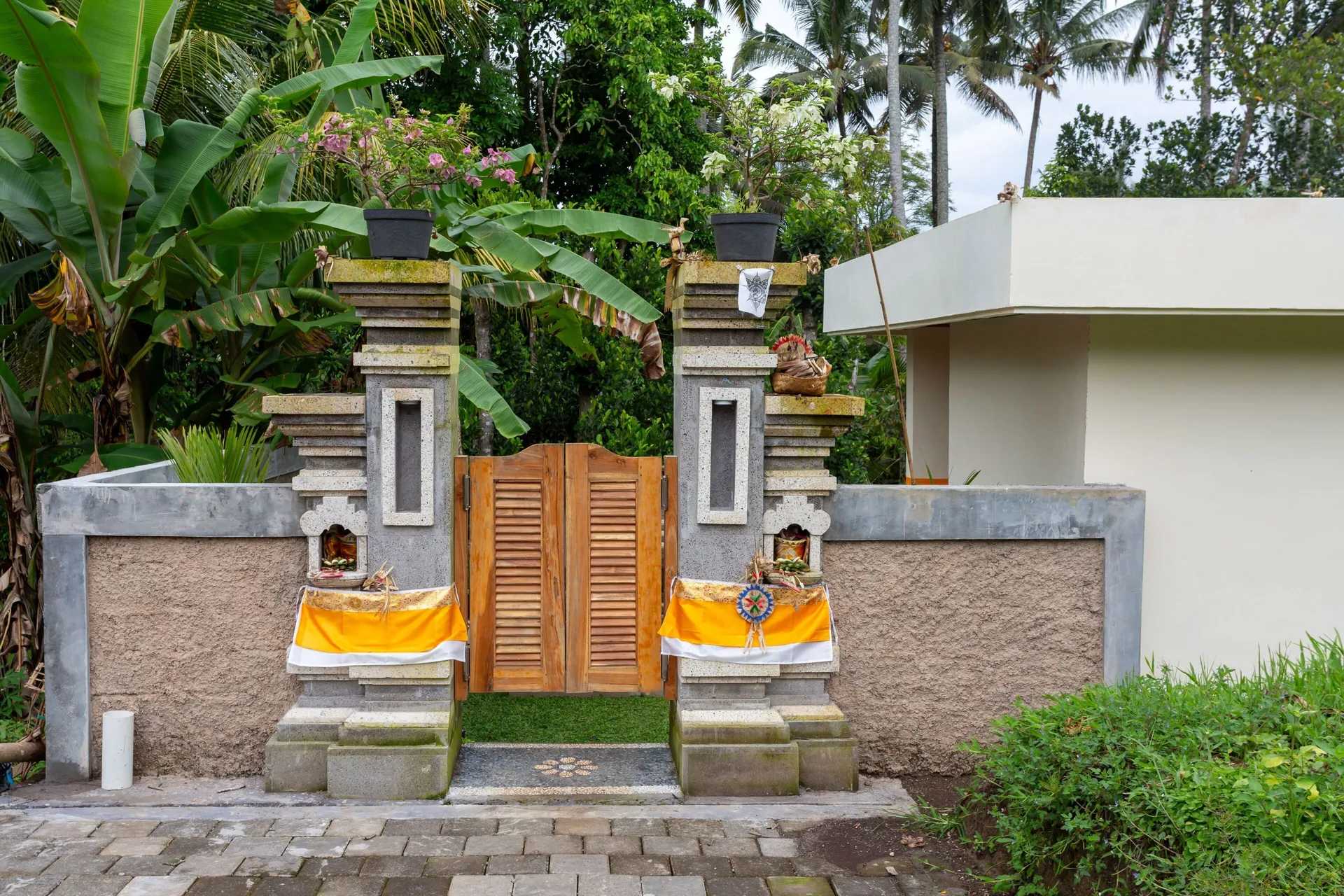 The carved wooden entrance gate to the property, flanked by two stone Balinese pillars dressed with yellow cloth