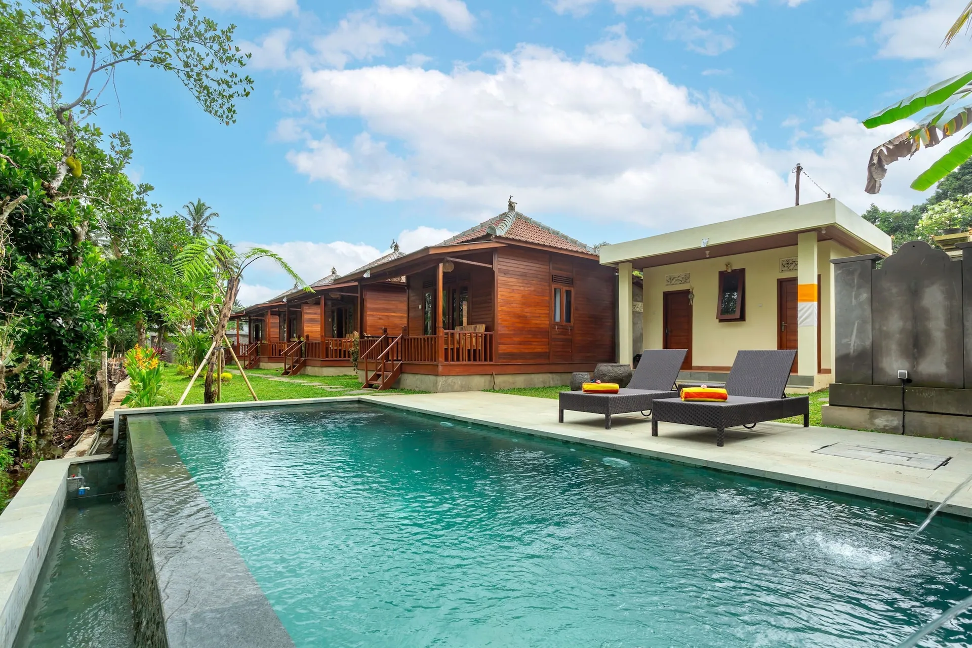 Sun loungers with orange towels on the pool terrace, the cabins and a bright sky behind