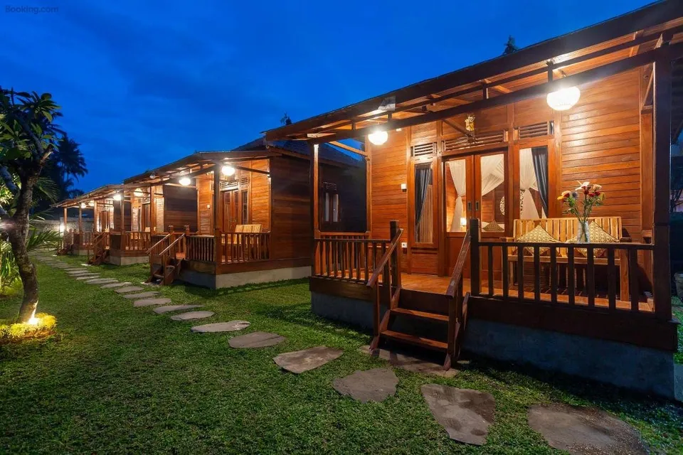 The row of four timber cabins at dusk under a deep blue sky, each veranda light on and a stone path leading past them