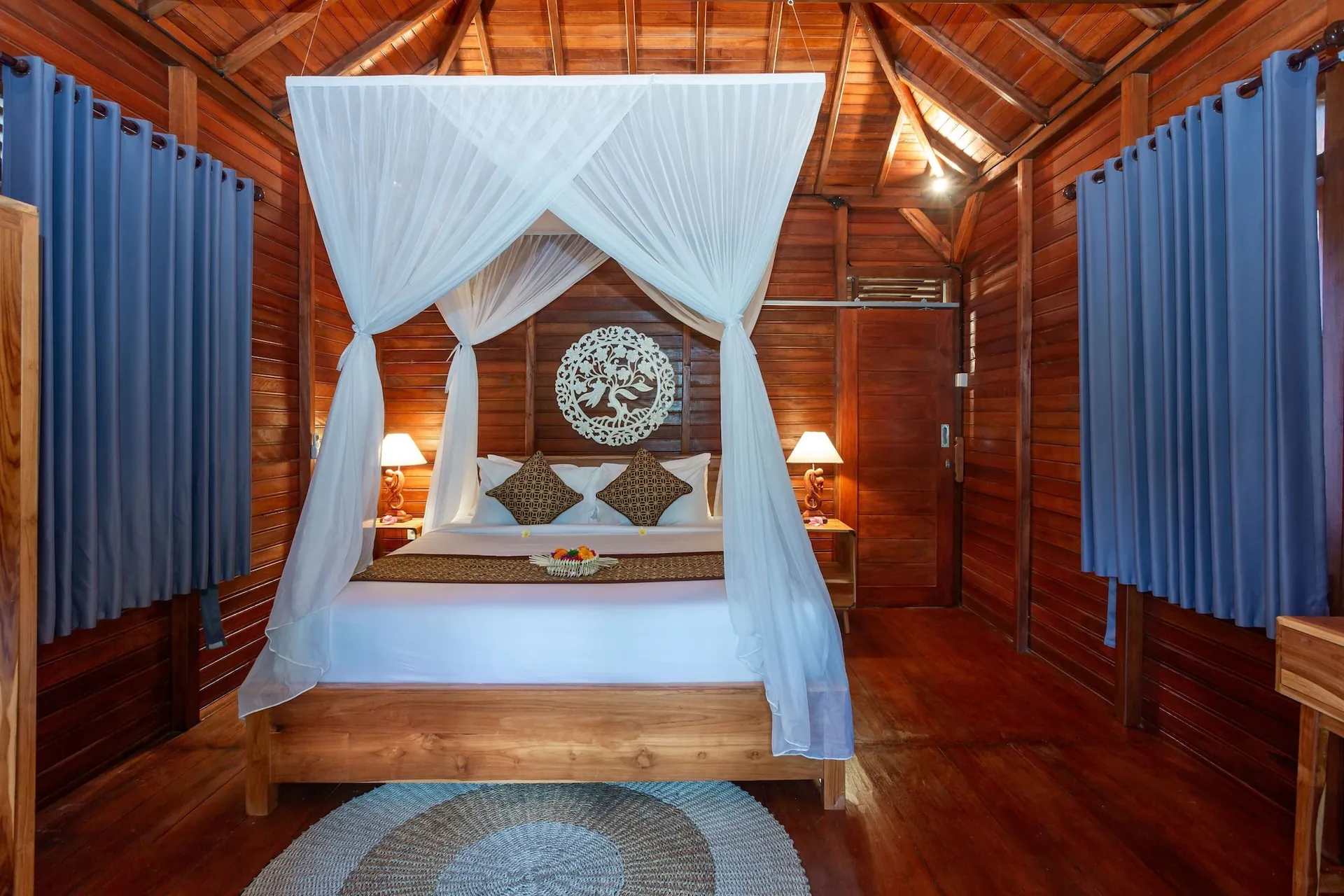 A four-poster bed seen head-on beneath a carved timber headboard panel, netting tied back at the corners