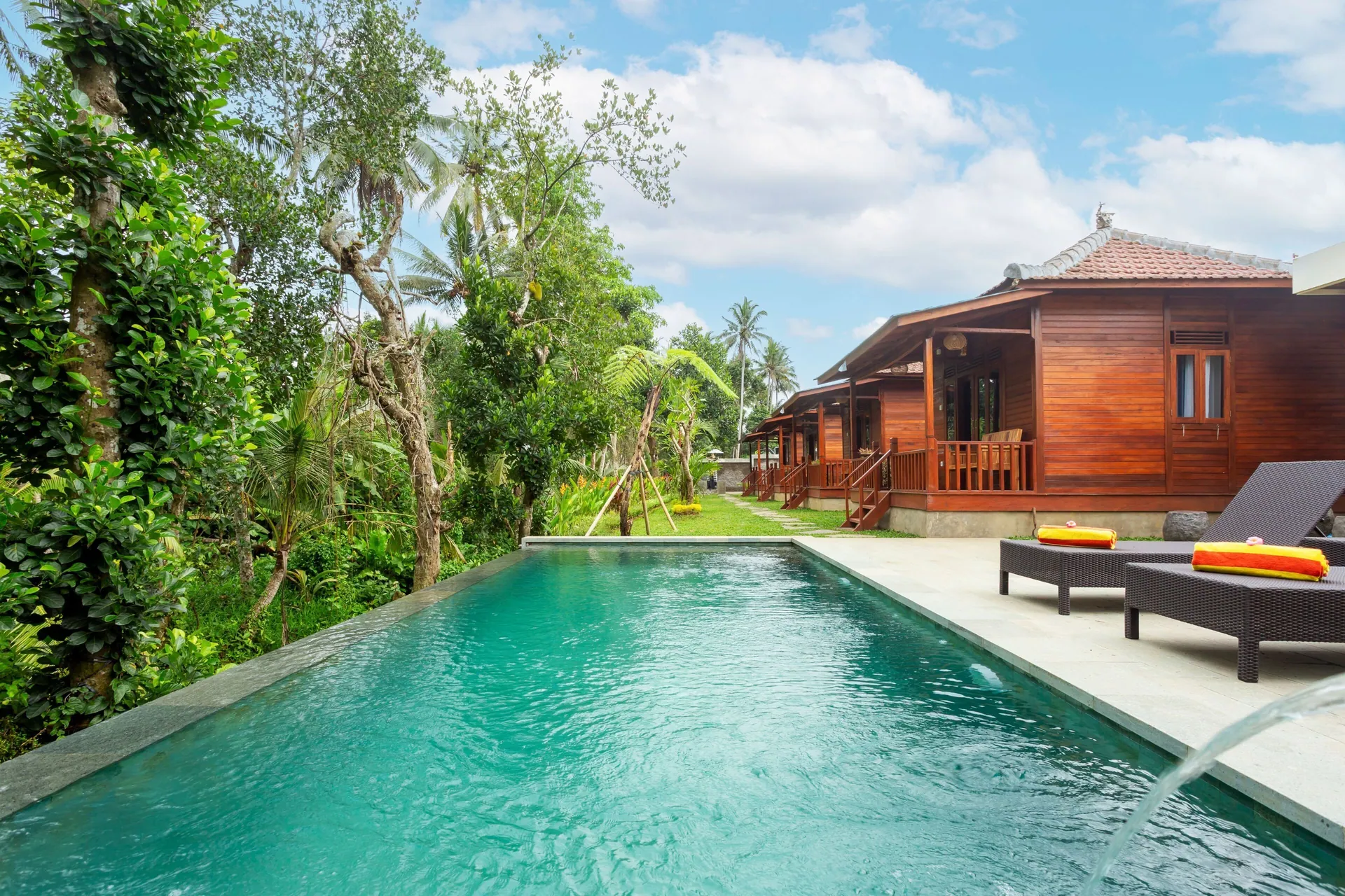 The long swimming pool at Pondok Naples Ubud in the morning, its water green against the timber cabins and the palms and banana trees behind them